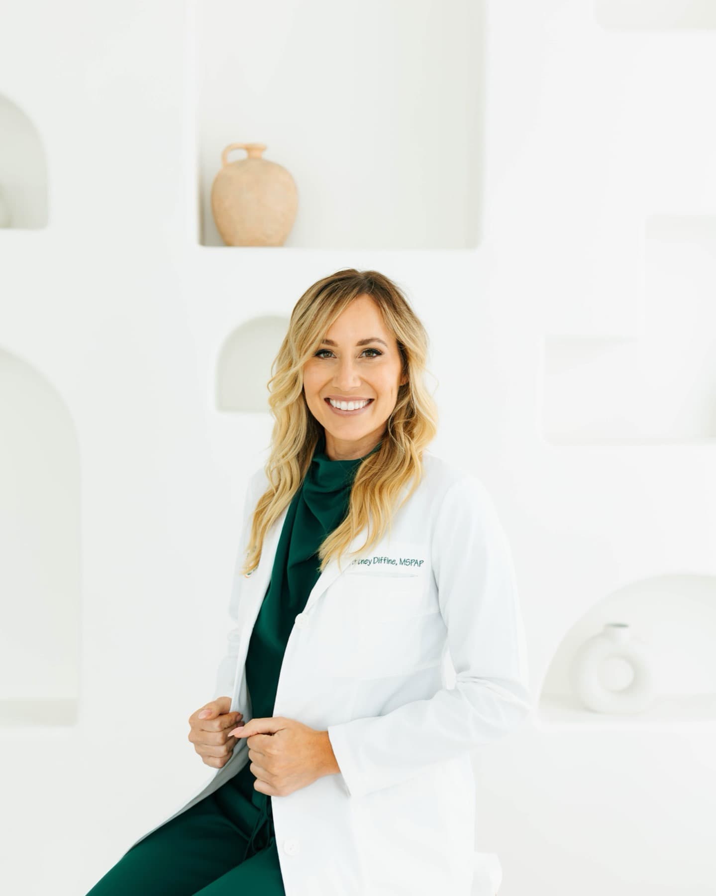 Brittney Diffiné, PA-C, in a white lab coat over emerald scrubs