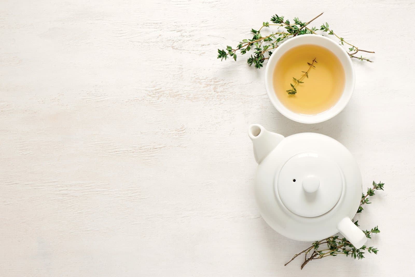 A white teapot and a cup of herbal tea with fresh thyme, seen from above